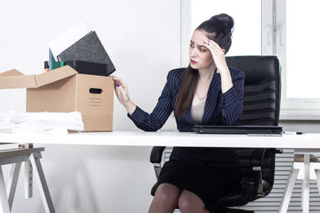 Dismissal. Dismissal box next to upset girl. Office worker has lost his job. Woman was upset when she found out about dismissal. Woman manager was fired. Girl behind office table. Job loss.の写真素材