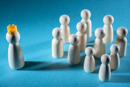 Business concept - conducting a master class. Man in crown conducts a master class. Someone speaks to the audience. Crown as a symbol of teacher's skill. Little white men on a blue backgroundの写真素材