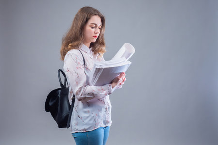 Woman student on gray background. Young girl with a backpack behind her back. The student has a lot...