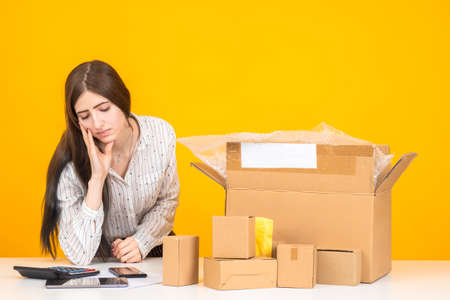 Sad woman next to a calculator. Girl considers her losses. Concept - boxes with personal belongings as a symbol of dismissal. The girl is upset by the dismissal. Woman considers loss from job lossの写真素材