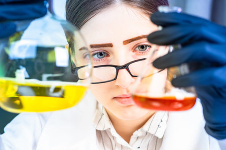 Lab technician examines test tubes. Girl compares liquids. Laboratory assistant face close up....