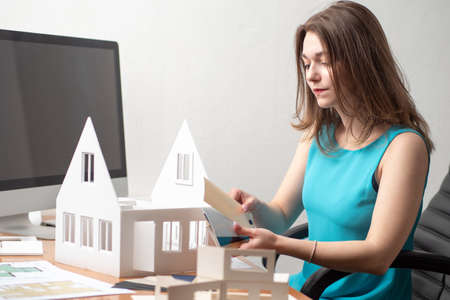 Young girl with a palette in her hands. Woman chooses the color of the building. Concept - designer thinks through the exterior of the house. Architectural design. Woman works as an interior designerの写真素材