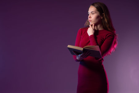 Portrait of a woman with a book in her hands. Girl on a dark purple background. She is standing...