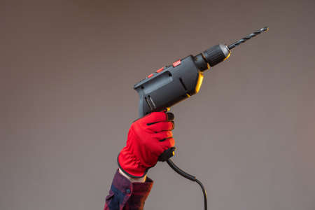 Hand with an electric drill. Construction electric tool. Hands in construction gloves. Electric drill on a dark background. Concept - drilling holes. Concept - sale of drills for construction.の写真素材