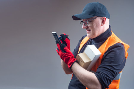 Courier with boxes and a smartphone in his hands. Courier in orange yolk. Courier uses application...