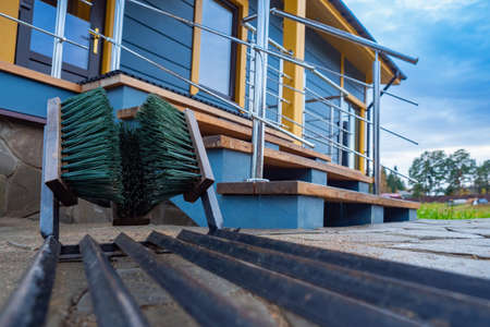 Shoe cleaning before entering the house. Cottage with a porch and Shoe brushes at the entrance. Maintaining cleanliness in a private home. Porch with metal railing. House in the countryside.の写真素材