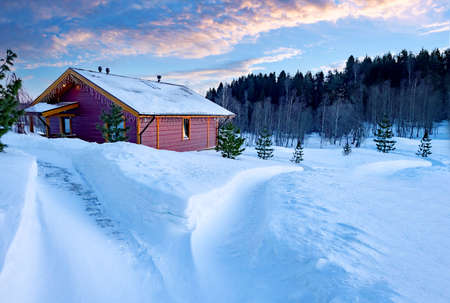 Wooden house at edge of forest. One-storey cottage in winter weather. Single private house near forest. Country house. Trail goes to cottage in middle of snowdrifts. Cottage on a sunny winter dayの写真素材