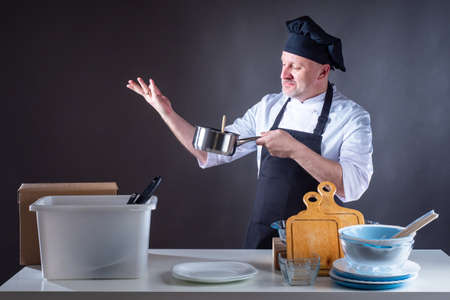 Chef man in restaurant kitchen. Cook is cooking something in a restaurant. Cook holds pan in his hands. Adult chef dissatisfied with taste. Cook doubts quality of the dish. Work in a restaurantの写真素材
