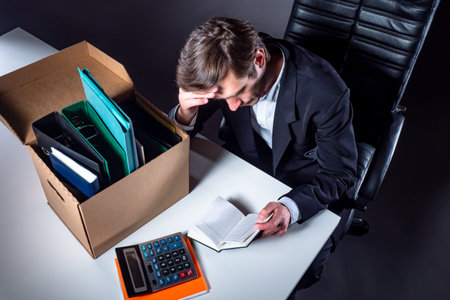 Unemployed man sits at table. Unemployed young man next to a carton box. Unemployed man leafs...