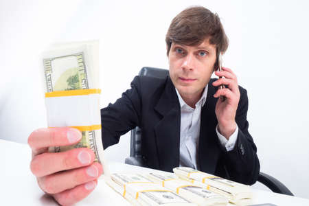 Man shows money to camera. Businessman holds money in his hands. Man holds out dollars to screen. Concept - businessman makes good money. Man with phone on white background. Human calculates savingsの写真素材