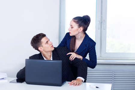 Love affair at work. Young business woman flirting with a man in office. Young couple workplace. Man and a woman look each other passionately. Woman touches hand of a man in cabinet. Flirting at workの写真素材