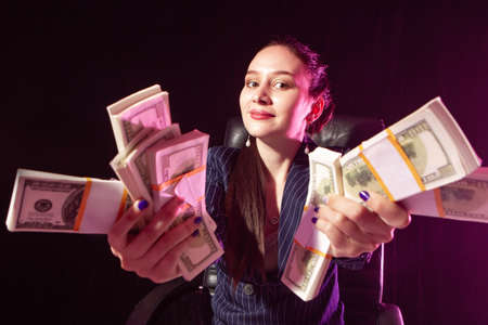Woman holds out money to camera. Concept - girl showing off about money. Woman demonstrates her earned money. Bundles of dollars in hands of a businesswoman. She made a lot of dollars.の写真素材