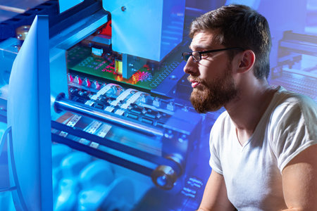 A man is studying the production process of a PCB. Concept - a man sets up a CNC machine. Engineer...