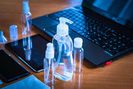 Various bottles with a dispenser on the table. Concept - an antiseptic is next to a laptop. Concept - disinfection gadgets. Cleaning bacteria after visiting the street. Using a sanitizer at work.の写真素材