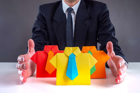 Company staff. Origami in form of office workers on table. Concept - joint activity company employees.  Manager manages company staff. Man in suit in backgroundの写真素材