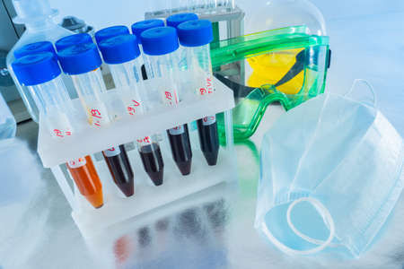 Covid. Test tubes with blood samples. Medical masks lie on table. Test tubes containing samples of infected Covid 19 blood. Positive result for coronavirus. Several test tubes on a laboratory benchの写真素材