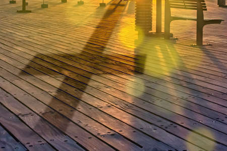 Reflection of the cross on the earth. Wooden embankment. Concept - religious cross casts a shadow. Sunset. Cross as a symbol of Catholicism. Concept - God is giving a sign. Silhouette.の写真素材