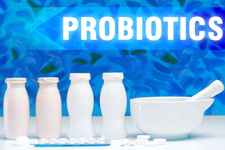 Probiotics in fermented milk products. Cooking yogurt with probiotics. Add pills to yogurt bottles. Plate for preparation of medicines. Inscription probiotics on the background of blue moleculesの写真素材