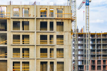 Two multi-story buildings are being built nearby. Construction of a new residential complex. Tower crane is working on building house. Concept - work in construction business. Building without facadeの写真素材