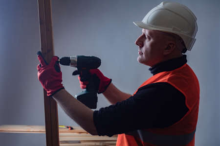 Builder tightens the screw. Man works with a screwdriver. Concept - work with an electric screwdriver. Process of assembling furniture. Connection of wood elements. Concept - furniture businessの写真素材