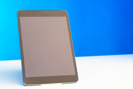 Technology device with an empty display. Tablet computer on a white table. Electronic tablet on a white and blue background. Tablet with space for text. Laptop with the screen off.の写真素材