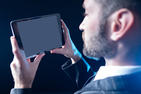 Man looks to planets. Portrait of a businessman with a tablet close-up. Guy with a gadget on a black background. Tablet with blank screen in ruins of a businessman. Concept - he speaks via video linkの写真素材