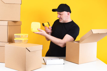 Warehouse worker with barcode reader. Cardboard boxes are on the table. Warehouse worker holds a plastic container in his hand. Man reads the code using a laser scanner. Shipment of goods from stockの写真素材