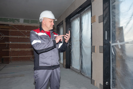 Construction materials ordering. Builder with a smartphone inside a building under construction. A...