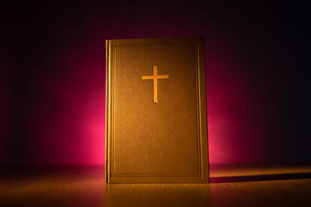 Religion and faith concept. Bible stands vertically on a wooden table. Bible is illuminated with a...