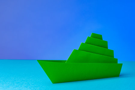 Paper boat on a blue background. Green multi-storey ship. Concept - loneliness. Lone ship close-up. Origami from paper. Problems and depression due to loneliness. Loneliness in personal life.の写真素材