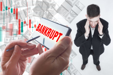 Bankruptcy. Guy holds his head. Man became bankrupt. Concept - going through a personal bankruptcy procedure. Inscription bankrupt on the phone screen. Falling money next to chart. Devastationの写真素材
