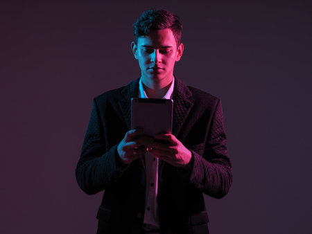 Young businessman with electronic tablet in his hands. Young man in a business suit with a tablet in his hands. Guy with an electronic gadget stands in the middle of the shot on a dark background.の写真素材