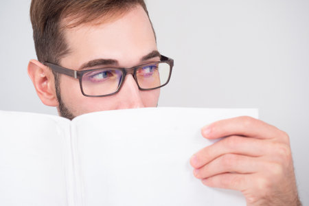 Man covers his face with papers. Lawyer with documents in hands. Guy with the glasses holds the lichty papers to his face. Young lawyer is scared of something. Concept career as a lawyer.の写真素材