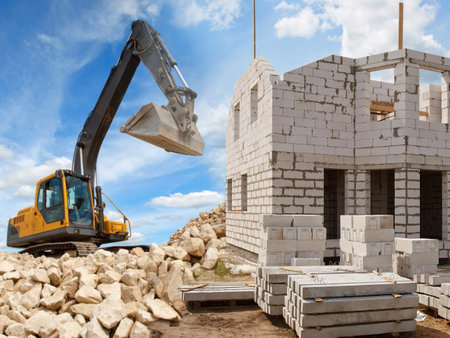 Demolition. Crawler Excavator. Concept - the demolition of illegal house. Crawler excavator demolishes an unfinished house. Excavator at a construction site. Unfinished house on the background of skyの写真素材
