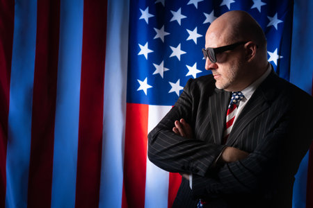 American politician folded his arms. Concept - politician speech. Man on background of USA flag. American politician in sunglasses. Man is building a political career in USA. Man working as lobbyist.の写真素材