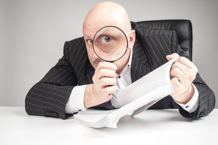 Man holds a magnifier next to his face. Concept - a lawyer is studying documents under a magnifying glass. Careful study of contracts. Businessman is reading a contract with a magnifier. Enlarged eyeの写真素材
