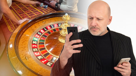 Game in online casino via phone. Concept is a casino application for a mobile phone. Distant gambling. Man on the background of the casino. Table with a tape measure in the background. Roulette Drumの写真素材