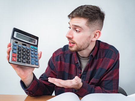 Guy shows a calculator. Dissatisfied man holds a calculator in his hands. Human shows the screen of a calculator. Concept - depression because of debts. Stress due to poor financial situation.の写真素材