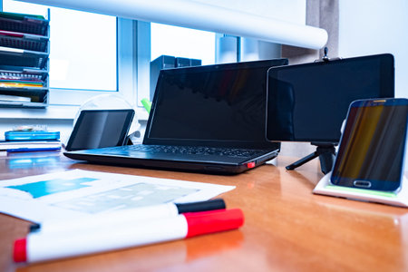 Desktop drawings of building on paper. Drawings of the room next to the laptop. Many gadgets on the...