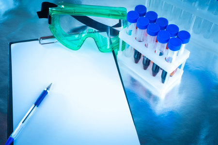 Empty sheet of paper next to test tubes. Place for an inscription. Virologist glasses next to blood...