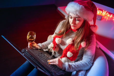 A girl in a red Santa hat wishes her friends a Merry Christmas online. Celebrating the new year During the pandemic. Christmas greetings in a virtual conference. Christmas on self-isolation.の写真素材