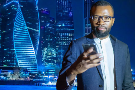 African American on background of evening skyscrapers. Young businessman downtown. Man in business suit looks at camera. Black businessman is calling someone. African businessman next to skyscrapersの写真素材