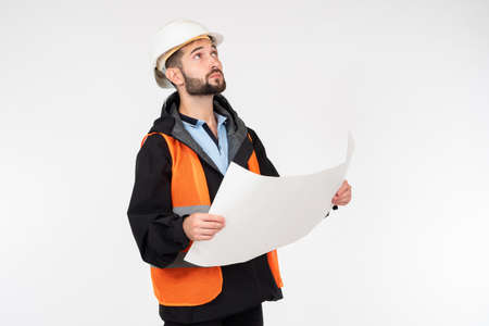 Builder with sheet of paper looks up. Construction worker is holding large sheet of paper. Man is dressed construction worker. Architect on light background. Concept - architect oversees constructionの写真素材