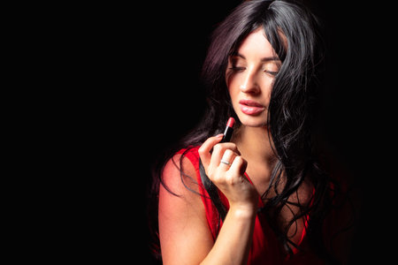 Makeup. Lipstick. Woman with lipstick on a black background. Girl applies makeup to herself. Passionate woman with lipstick. The woman in the red outline is putting makeup on herself.の写真素材
