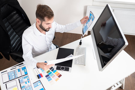 Application development. Mockups of mobile apps on paper. Phone application developer. Concept - application development company. Man checks work of web designers. Web development studio.の写真素材