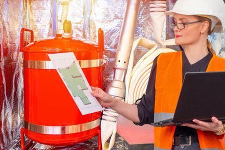 Fire safety. Woman works a fire inspector. Girl checks equipment to extinguish flame. Woman next to extinguishing equipment. Fire inspector with a laptop in his hands. Selling extinguishing equipmentの写真素材