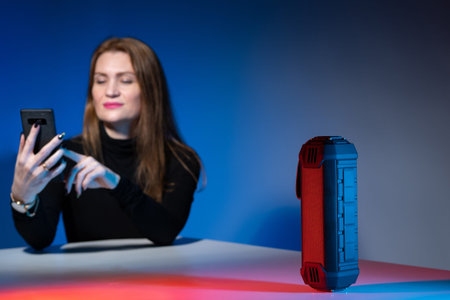 A smiling woman controls a speaker from her smartphone. A girl with a mobile phone on the background...
