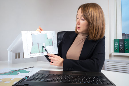 Presentation of the construction project online. A female architect demonstrates a building plan in front of a laptop camera. Remote real estate transactions. Remote sale of an apartment.の写真素材