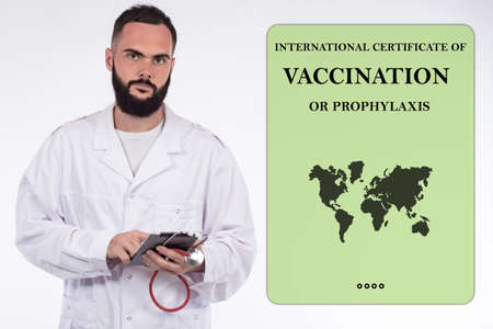 The doctor issues an international certificate of vaccination or prevention of coronavirus. The male doctor next to the form of the immune passport. Medical certificate of immunity to Covid-19.の写真素材