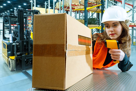 Girl holds a barcode scanner. Laser scanner is pointing at barcode. Concept - issuance of online orders. Young woman works in a warehouse. Checks the box by barcode. Concept - warehouse business.の写真素材